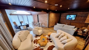 A modern living room with a large sofa set, a coffee table, and a television mounted on a brick wall. - Château Suisse Boutique Hotel (Campos do Jordão)