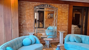 A modern living room with a curved blue sofa, a wooden coffee table, and a large mirror reflecting the room. - Château Suisse Boutique Hotel (Campos do Jordão)