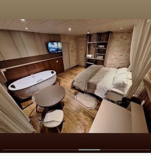A modern bedroom with a large bed, a separate bathtub, a small round table, and a television. - Château Suisse Boutique Hotel (Campos do Jordão)