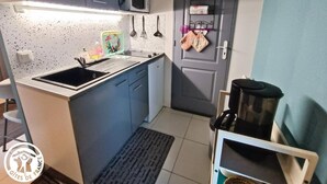 A compact kitchen with a sink, microwave, and a door with a shelf above it. - Gîtes de France® - Le Cocon (PRAYSSAC)