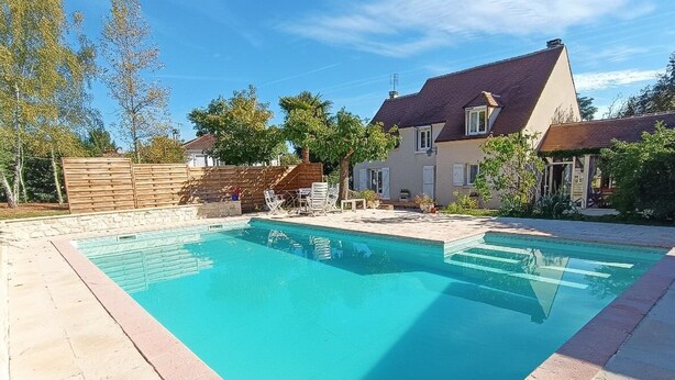 A rectangular swimming pool with a tiled deck, surrounded by a wooden fence and a house with a sloped roof. - Gîtes de France® - Le Cocon (PRAYSSAC)