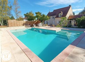 Una piscina rettangolare con bordo piastrellato, circondata da una recinzione in legno e una casa con tetto a falde.