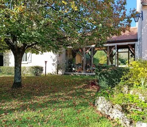 Une maison dotée d’un espace extérieur couvert, d’un arbre et d’un jardin.