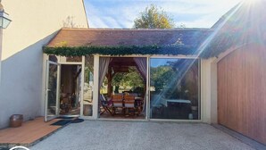 A covered patio area with a table and chairs, a wooden bench, and a pergola with vines. - Gîtes de France® - Le Cocon (PRAYSSAC)