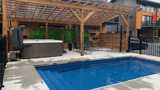 A swimming pool with a wooden pergola overhead, a hot tub, and outdoor seating.