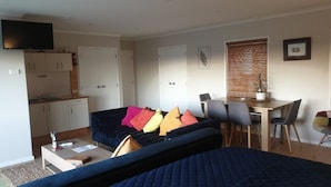 A compact living space with a sofa, a dining table, a TV, and a kitchenette.