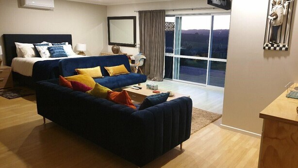 A modern hotel room with a large bed, a sofa, and a desk. There is a large window with a view of the outdoors.