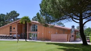 A wooden building with a large garage, a covered parking area, and a well-maintained lawn. - Apartment for 4 people, on the Lacanau Ocean golf course (LACANAU OCEAN)