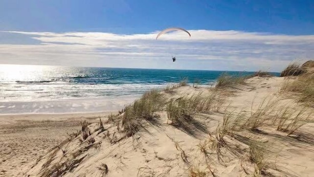 A beach with sand dunes and a person paragliding in the distance. - Apartment for 4 people, on the Lacanau Ocean golf course (LACANAU OCEAN)