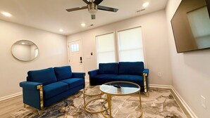 Un salon avec deux canapés bleus, une table basse ronde, un ventilateur de plafond et un grand miroir au mur.