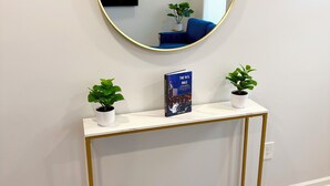 Une console blanche aux pieds dorés, un miroir rond avec un cadre doré et deux plantes en pot.