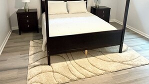 Un lit à baldaquin avec un cadre foncé, deux tables de chevet avec des lampes, un tapis de couleur claire et un ventilateur de plafond.