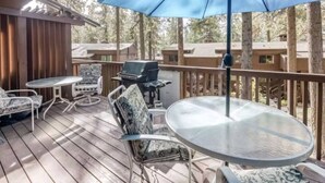 Une terrasse dotée de mobilier d’extérieur, d’un barbecue et d’un grand parasol.