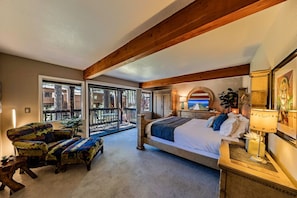 A bedroom with a large bed, a desk, a chair, and a balcony with a view of the outside.