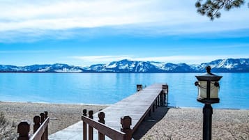 Eine Holzstege führt zu einem Sandstrand mit Bergen im Hintergrund.