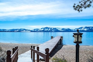 A wooden pier leading to a sandy beach with a mountain backdrop.