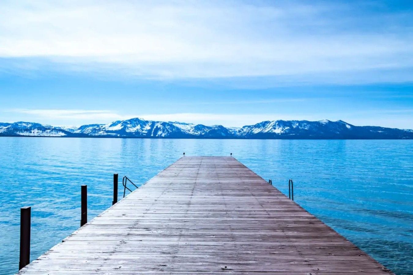 Une jetée en bois s’étendant sur une étendue d’eau calme, avec une chaîne de montagnes en arrière-plan.