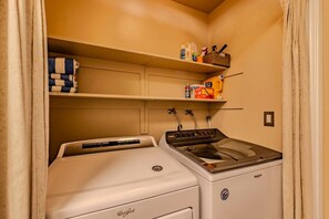 A compact laundry room with a front-loading washer and dryer, a shelf with cleaning supplies, and a towel rack. - Pinewild Retreat | Sauna, Decks & Beach | Sleeps 6 (Zephyr Cove)