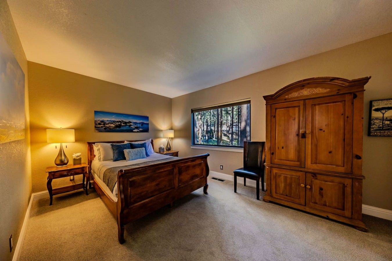 Un dormitorio con una cama de madera, dos mesitas de noche con lámparas, un ventanal con vistas a árboles y un armario de madera.
