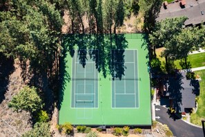 An aerial view of a tennis court surrounded by trees and a parking area.