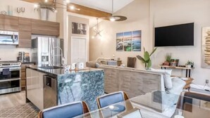 A modern kitchen with built-in appliances, a dining area with a glass table, and a living space with a TV and artwork. - Pinewild Retreat | Sauna, Decks & Beach | Sleeps 6 (Zephyr Cove)