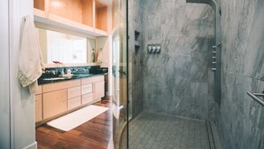 A modern bathroom with a glass-enclosed shower, marble walls, and wooden cabinetry. - Oceanfront Paradise: Breathtaking 3bd/2ba with Panoramic Views of Hilo Bay (Hilo)
