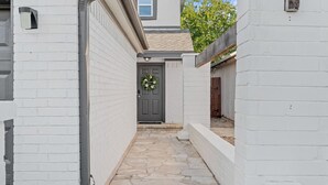 A narrow stone pathway leading to a dark grey door with a wreath, flanked by white brick walls.