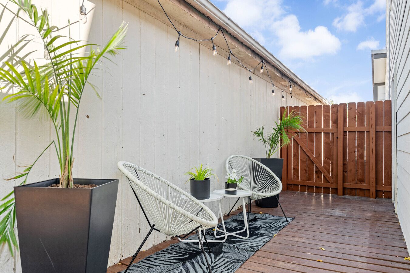 Une terrasse avec deux chaises en osier blanc, une petite table ronde et des plantes en pot.