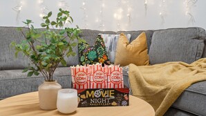 A cozy living room with a grey sofa, a small table with a plant, popcorn, and a movie night sign.