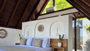 Een slaapkamer met een houten bed, een witte muur met decoratieve details en uitzicht op het buitenlands landschap door een glazen deur.