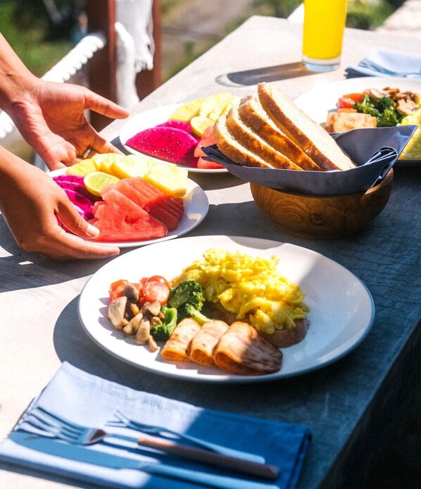 A picnic table with plates of food, including fruits, vegetables, and a bowl of bread.