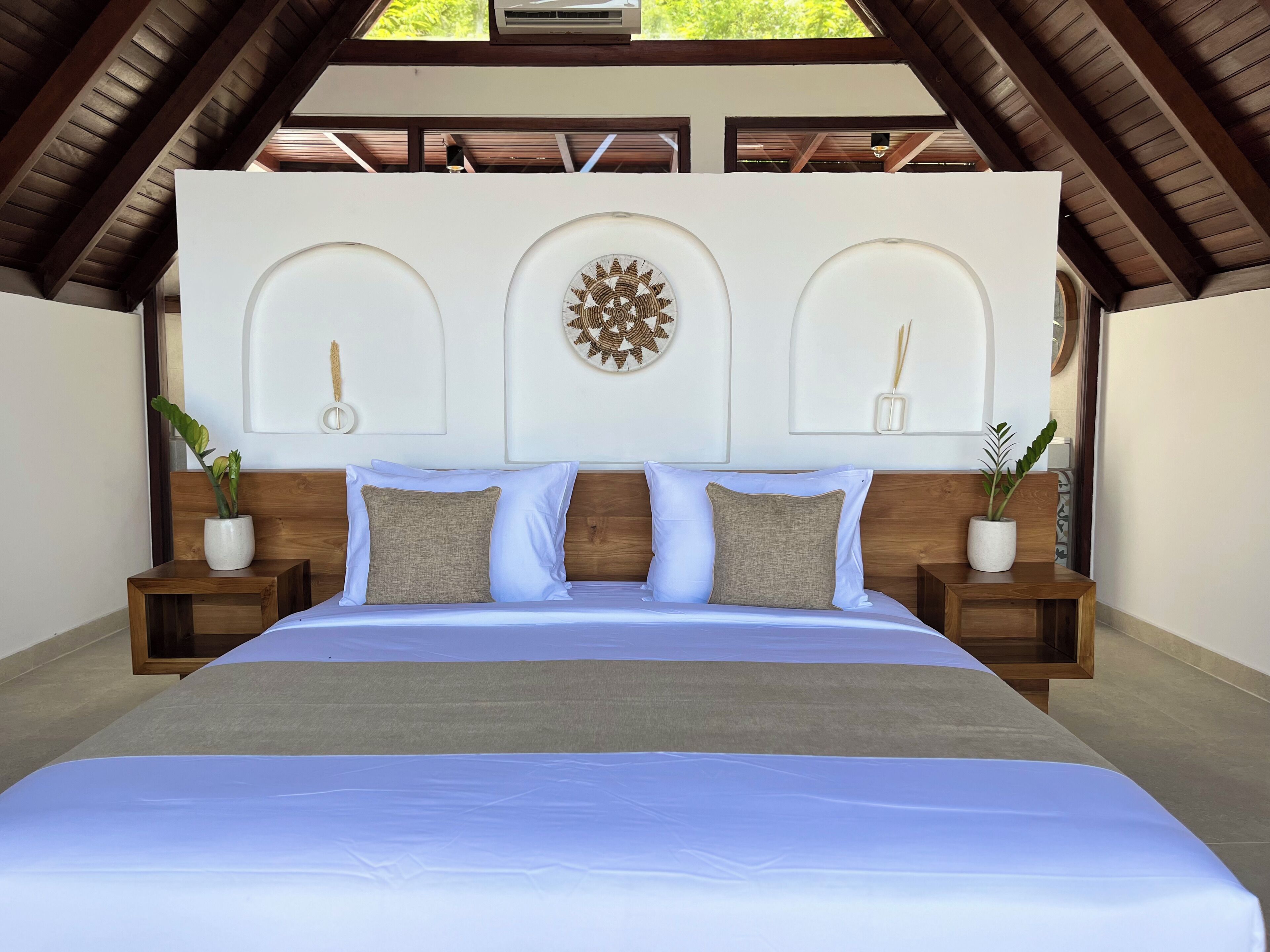 A bedroom with a large bed, wooden headboard, and two nightstands with potted plants.