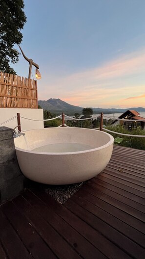 Un jacuzzi grande y redondo al aire libre sobre una terraza de madera, con vistas a montañas y una valla de madera al fondo.
