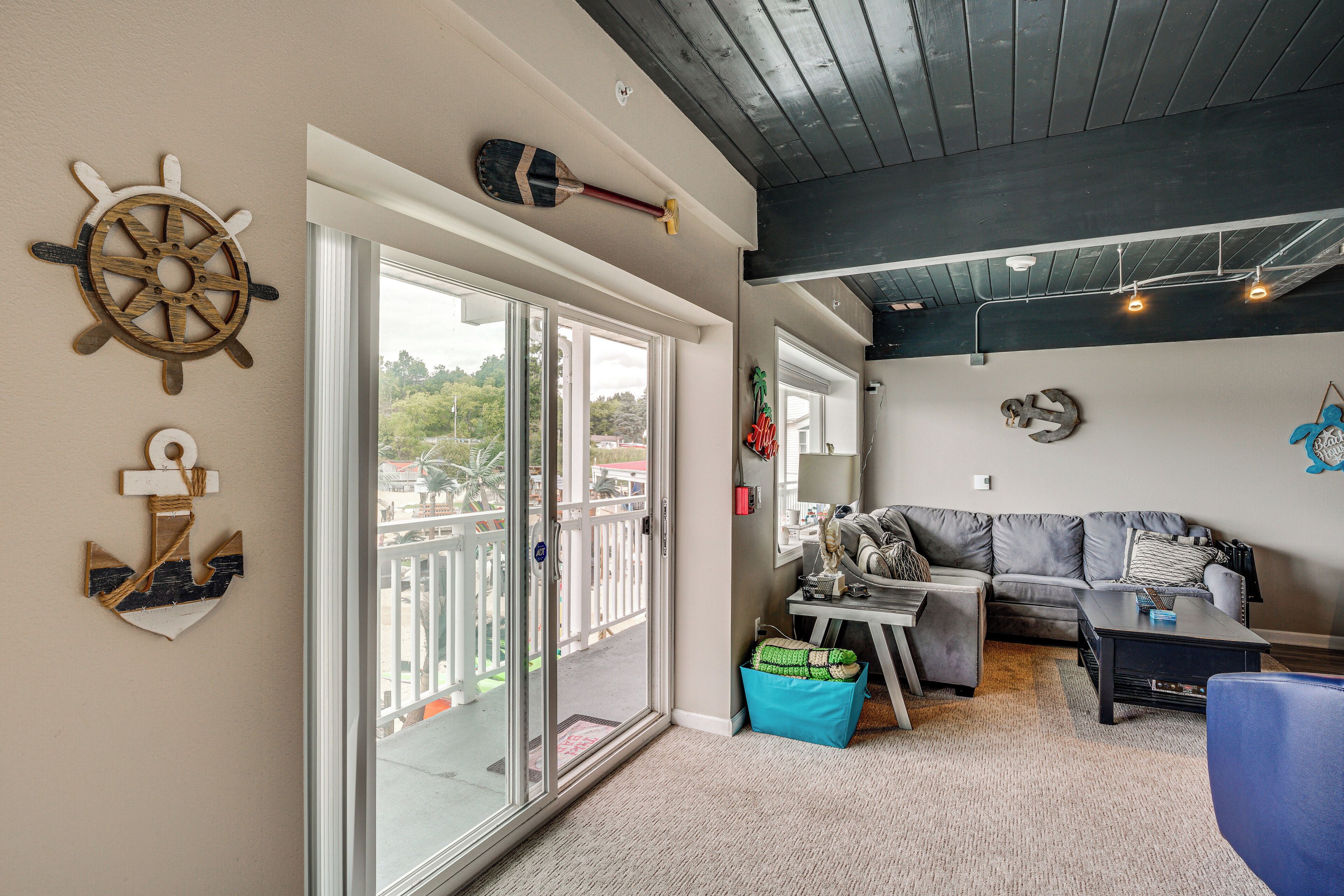 A living room with a sliding glass door leading to a balcony, a gray sofa, a coffee table, and nautical-themed wall decor.