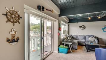 A living room with a sliding glass door leading to a balcony, a gray sofa, a coffee table, and nautical-themed wall decor.