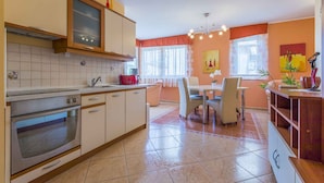 A kitchen with a built-in oven, a dining area with a table and chairs, and a window with curtains. - Holiday apartment with air conditioning and Internet access (Dramalj)
