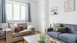 Olohuoneessa on beige värinen sohva, harmaa sohva ja puinen sohvapöytä, jonka päällä on koriste-esineitä.