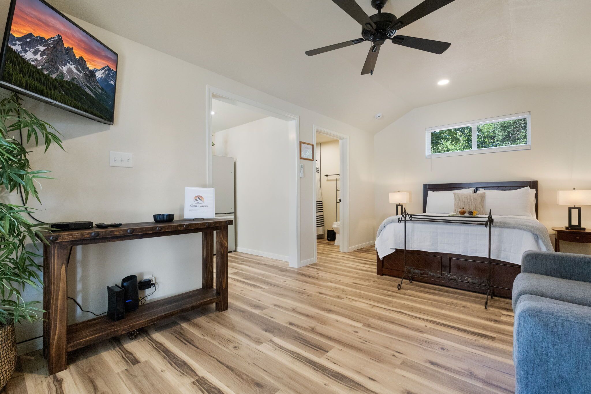 A bedroom with a bed, bedside tables, a ceiling fan, a TV, and a window.