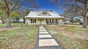 A single-story house with a porch, a stone pathway leading to the entrance, and a lawn with trees. - The Country Haus: Quaint Home 1 Mile From Downtown (Fredericksburg)