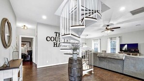 A modern living room with a spiral staircase, a grey sofa, and a large mirror on the wall. - The Country Haus: Quaint Home 1 Mile From Downtown (Fredericksburg)