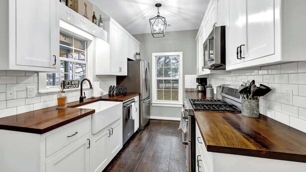 A modern kitchen with white cabinets, a wooden countertop, stainless steel appliances, and a window with a view of trees. - The Country Haus: Quaint Home 1 Mile From Downtown (Fredericksburg)