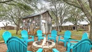 A rustic outdoor seating area with a stone fire pit surrounded by turquoise Adirondack chairs. - The Country Haus: Quaint Home 1 Mile From Downtown (Fredericksburg)