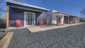 A row of cabins with sliding glass doors, red Adirondack chairs, and a gravel driveway. - Pop 1: Hot-tub + Close to Main St (Fredericksburg)