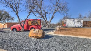 A red vintage truck parked on a gravel driveway, a wooden stump, and a white building with a window and door. - Pop 1: Hot-tub + Close to Main St (Fredericksburg)