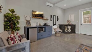 A modern living room with a grey sofa, a dining area with a blue cabinet, and a decorative plant. - Pop 1: Hot-tub + Close to Main St (Fredericksburg)