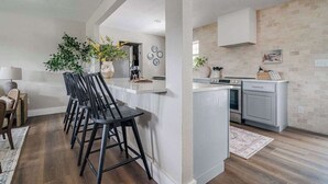 A modern kitchen with white cabinetry, a central island, and a dining area with black bar stools. - 108 Wisteria Dr (Fredericksburg)