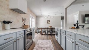 A modern kitchen with light blue cabinets, a central island, and a dining area with a chandelier. - 108 Wisteria Dr (Fredericksburg)