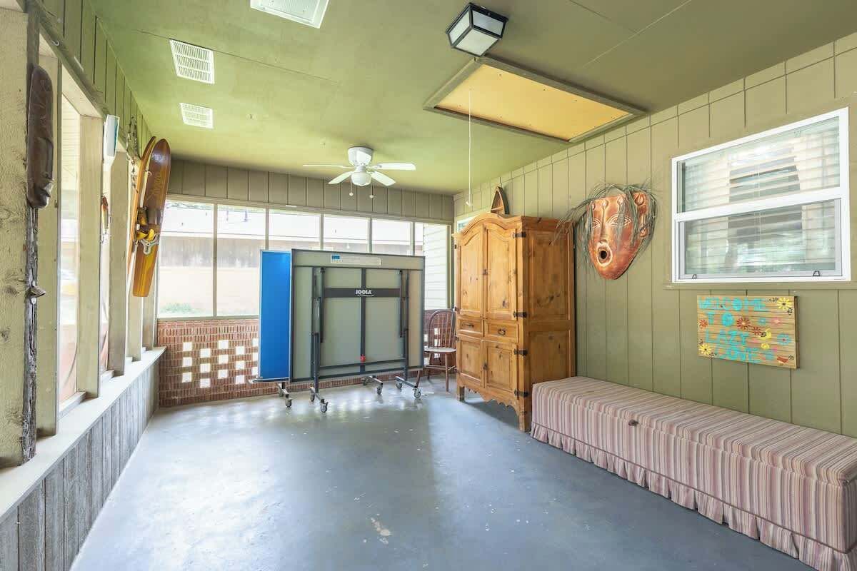 Una habitación con un banco de madera, un armario, un ventilador de techo y una ventana con persianas.