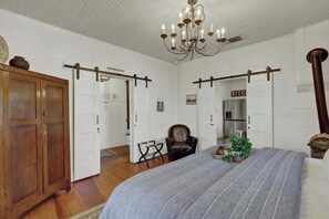 A bedroom with a large bed, a chandelier, a wardrobe, and a door leading to another room. - Victorian Escape-pool & Hot Tub! (Fredericksburg)
