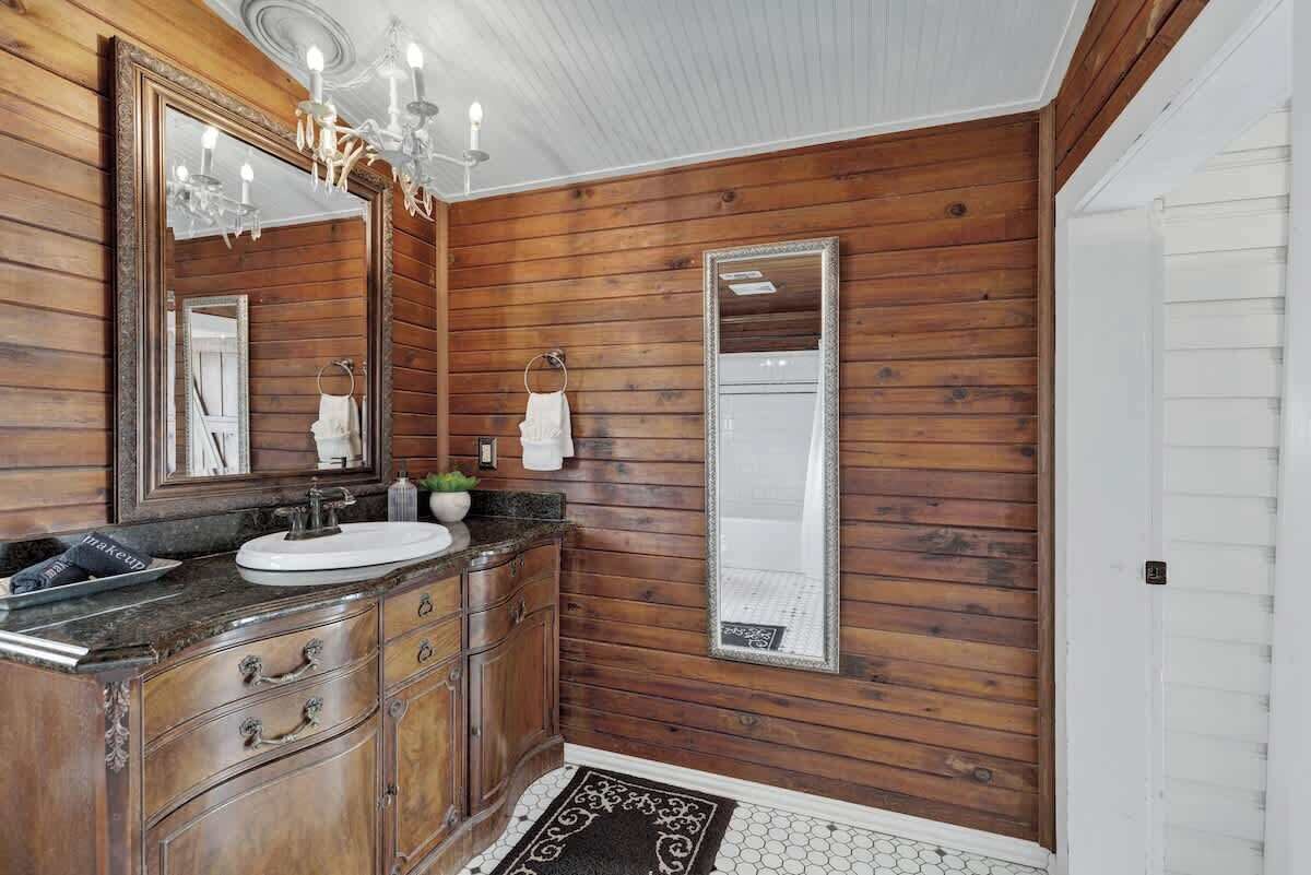 Un baño con paneles de madera, tocador, lavabo y espejo grande.